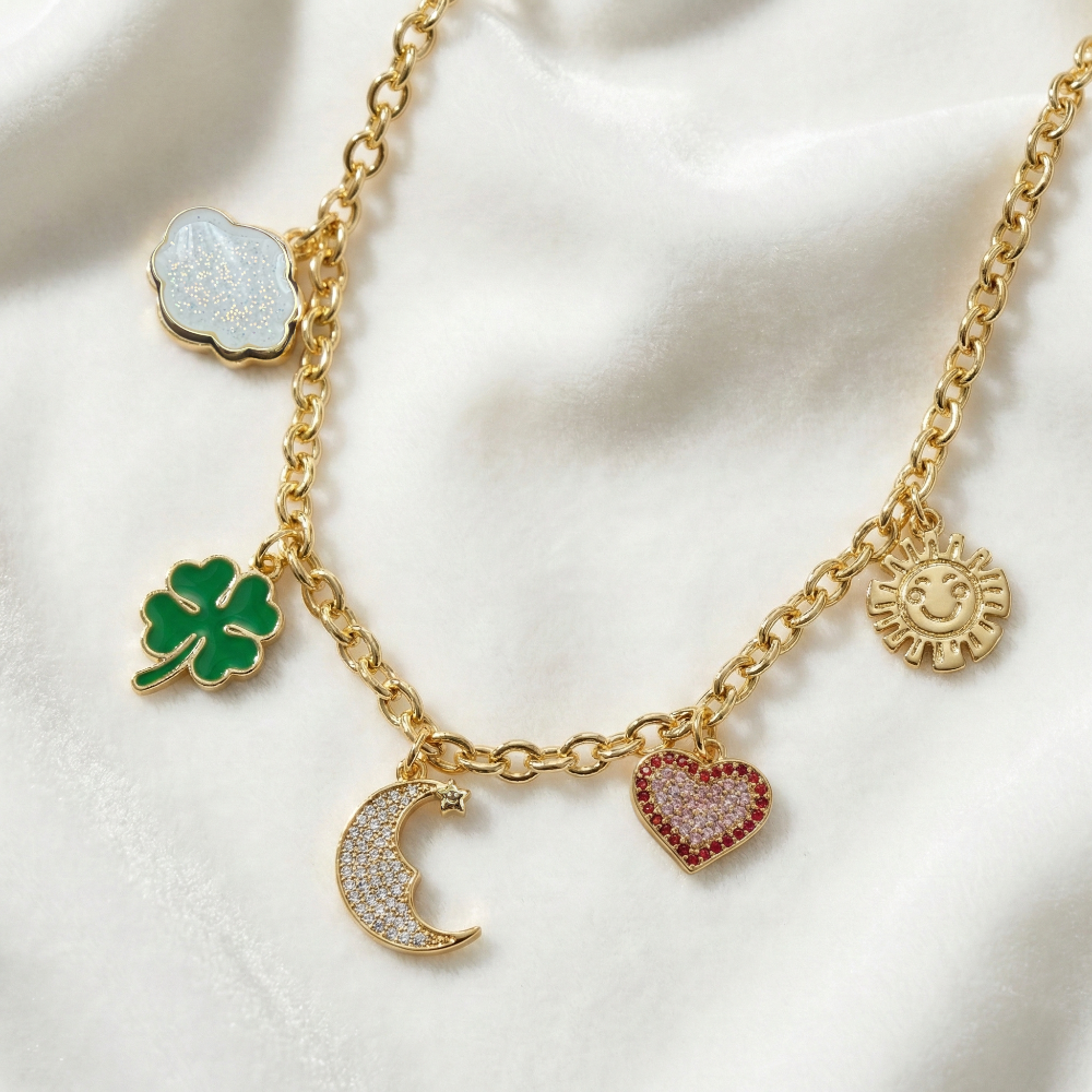 Necklace with various Care Bears Belly Badge charms including a cloud, four-leaf clover, a moon, heart and sun on a white velvet fabric background by Couture Kingdom