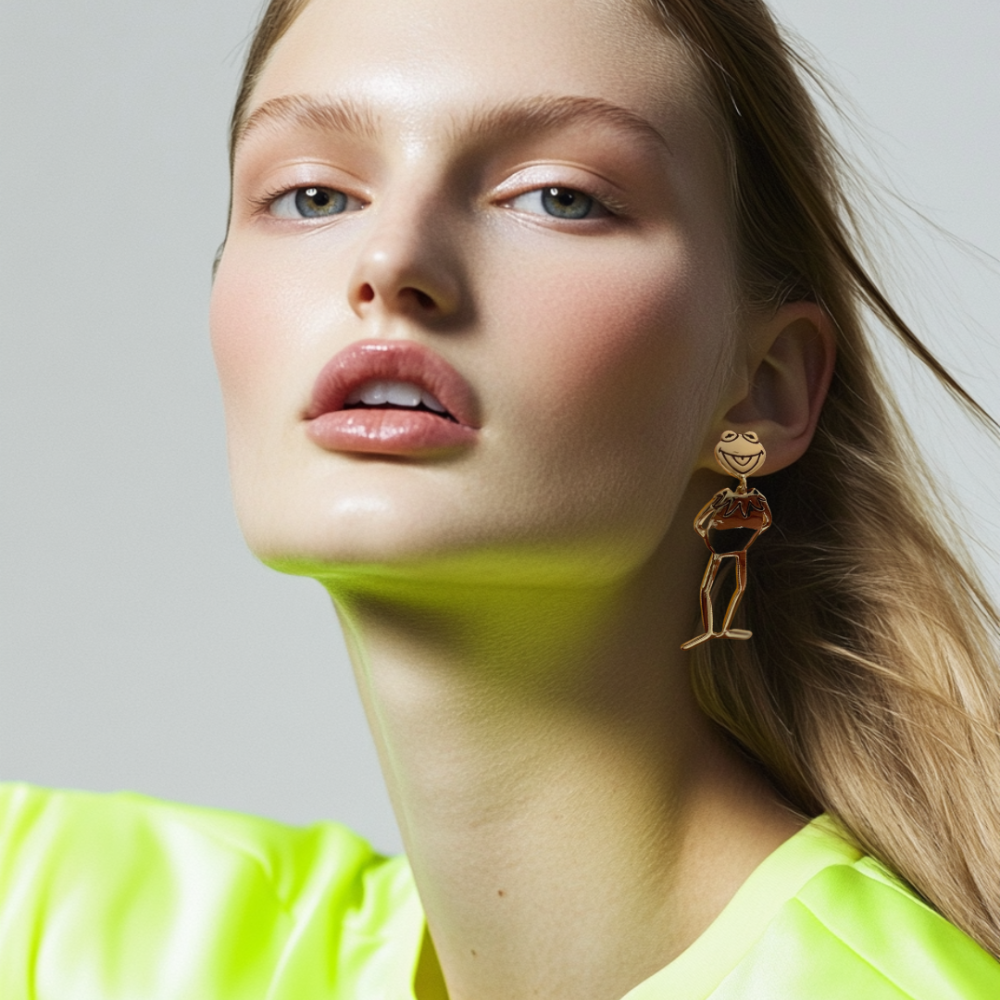 Close-up of a person wearing a bright yellow shirt and yellow gold plated Kermit the frog full body drop earrings by Couture Kingdom against a neutral background