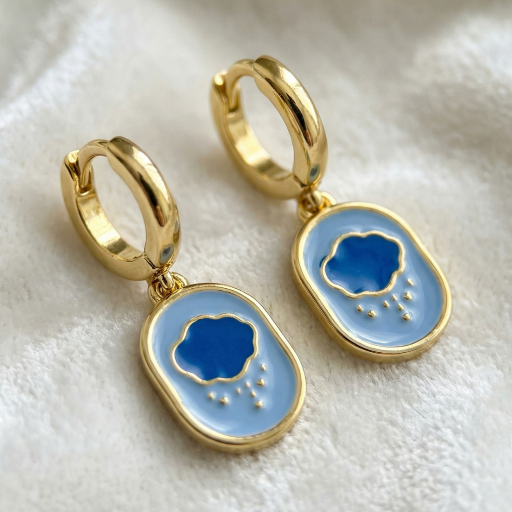 Yellow gold mini hoop earrings with Care Bears Grumpy Bear enamel belly badge icon charm hanging from bottom on a white furry fabric background by Couture Kingdom