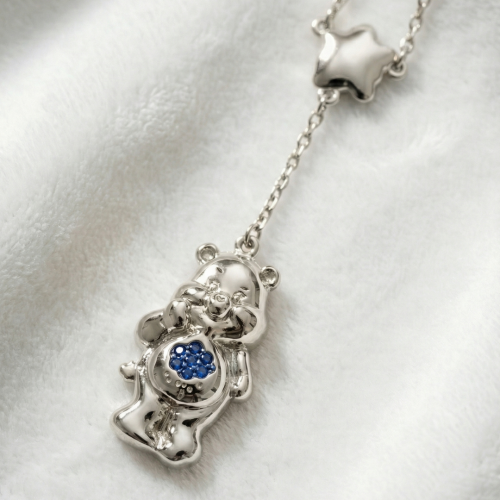 White gold plated Care Bears Grumpy  bear pendant necklace with a star buddie and blue crystal cloud as belly badge by Couture Kingdom on a white furry fabric background