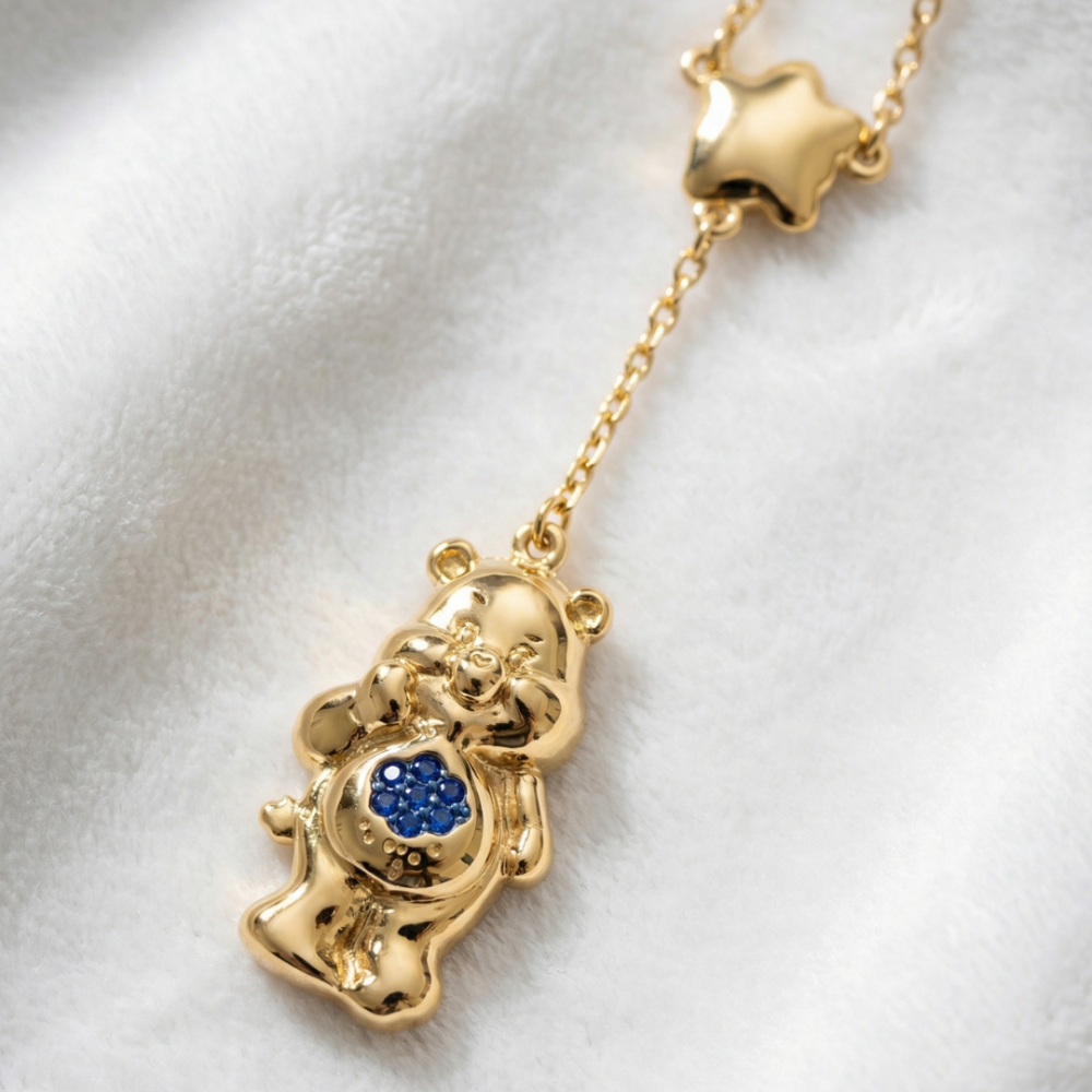 Yellow gold plated Care Bears Grumpy  bear pendant necklace with a star buddie and blue crystal cloud as belly badge by Couture Kingdom on a white furry fabric background