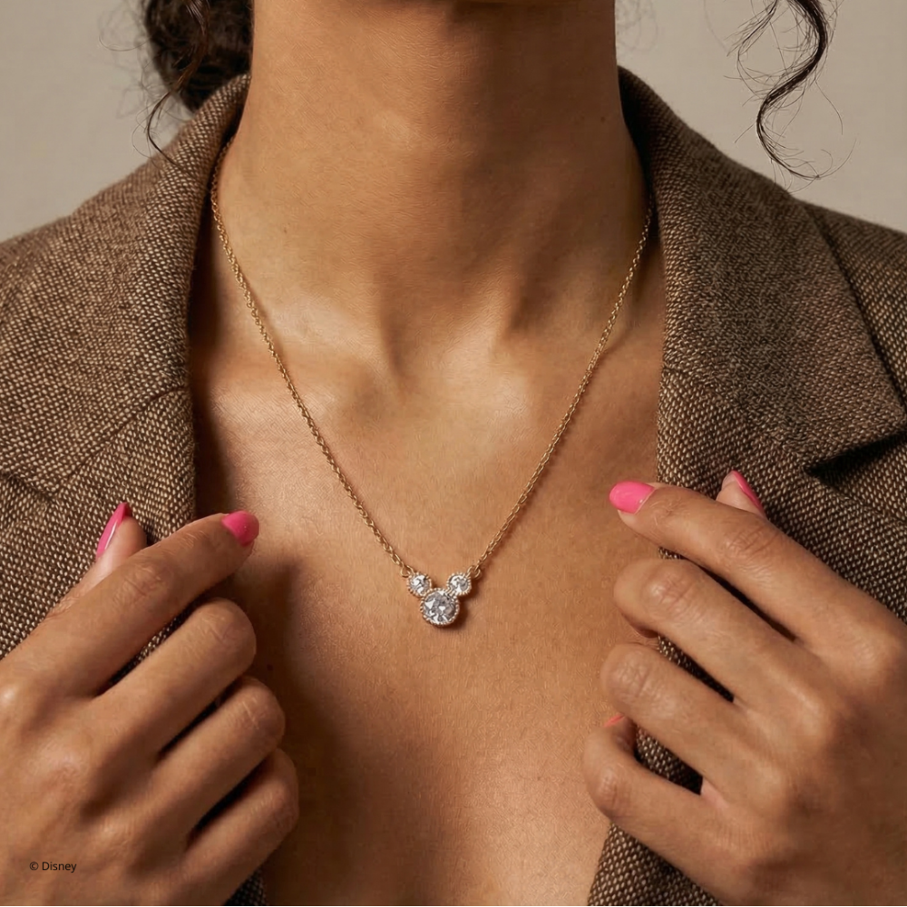 Woman wearing a gold necklace with a crystal Mickey Mouse pendant against a neutral background