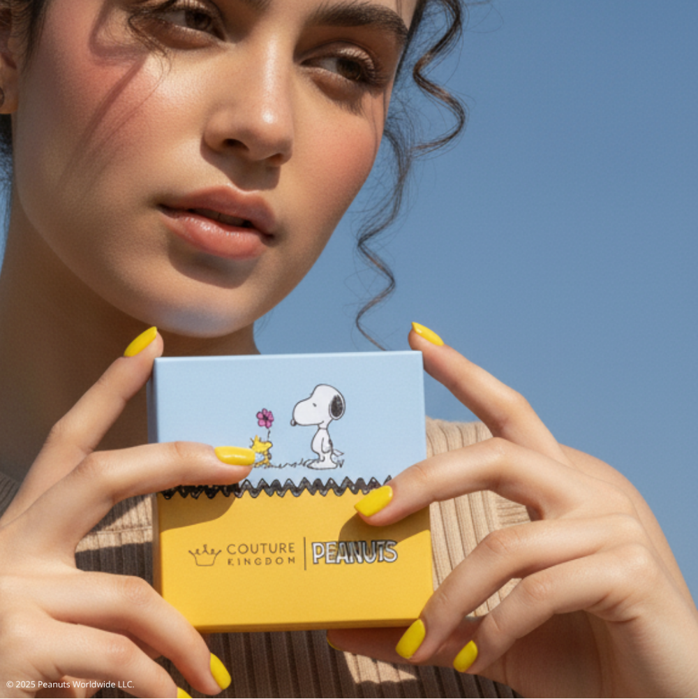 Person holding a small square jewellery box packaging with Snoopy peanuts design against a clear blue sky