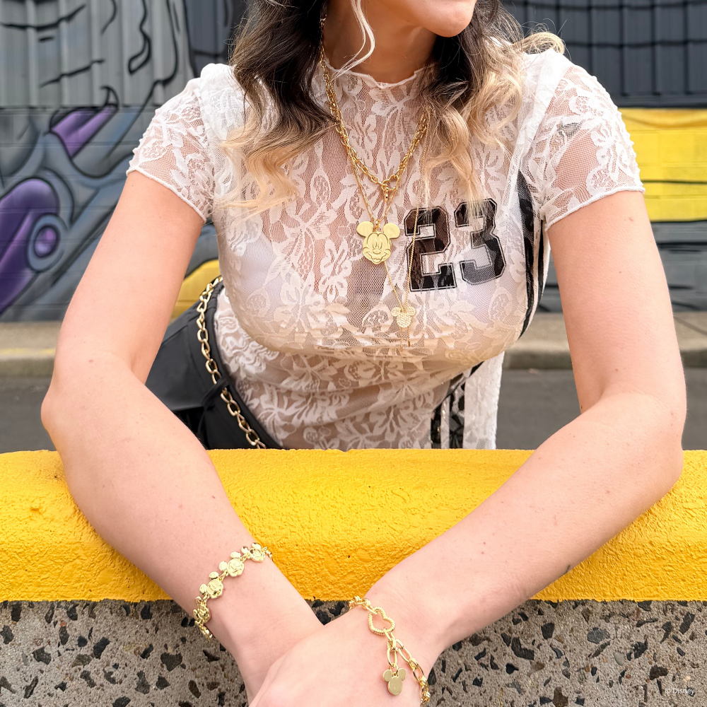 Disney_Mickey_Mouse_Jewellery_By_Couture_Kingdom_on_model wearing a white lace top with '23' sitting on a yellow bench.