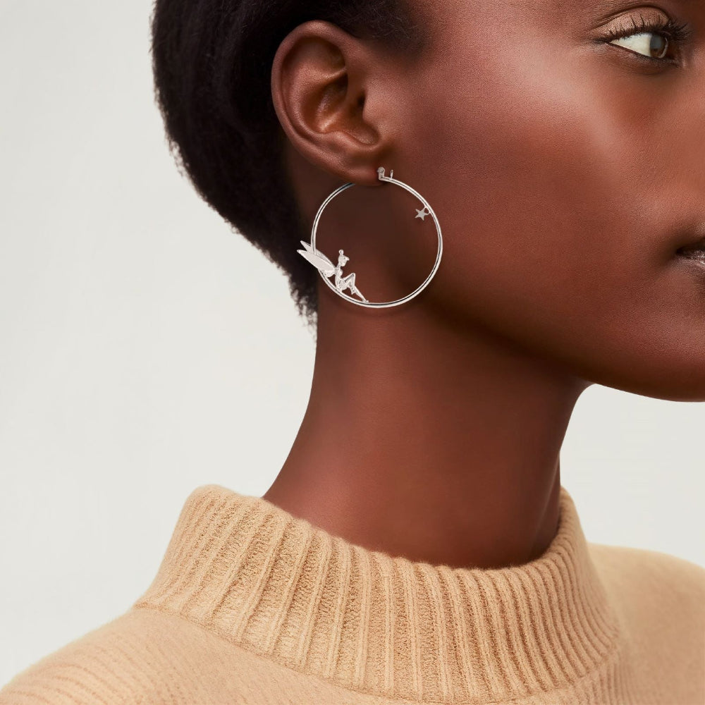 White gold plated large hoop earrings with Disney Tinker Bell sitting inside the hoop by Couture Kingdom worn on a model with a beige top against a neutral background