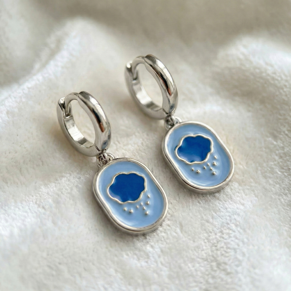 White gold mini hoop earrings with Care Bears Grumpy Bear enamel belly badge icon charm hanging from bottom on a white furry fabric background by Couture Kingdom