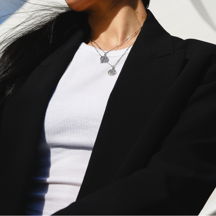 Person wearing a black blazer over a white shirt with a silver Avengers necklace layered with a silver Black Panther Necklace by Couture Kingdom.