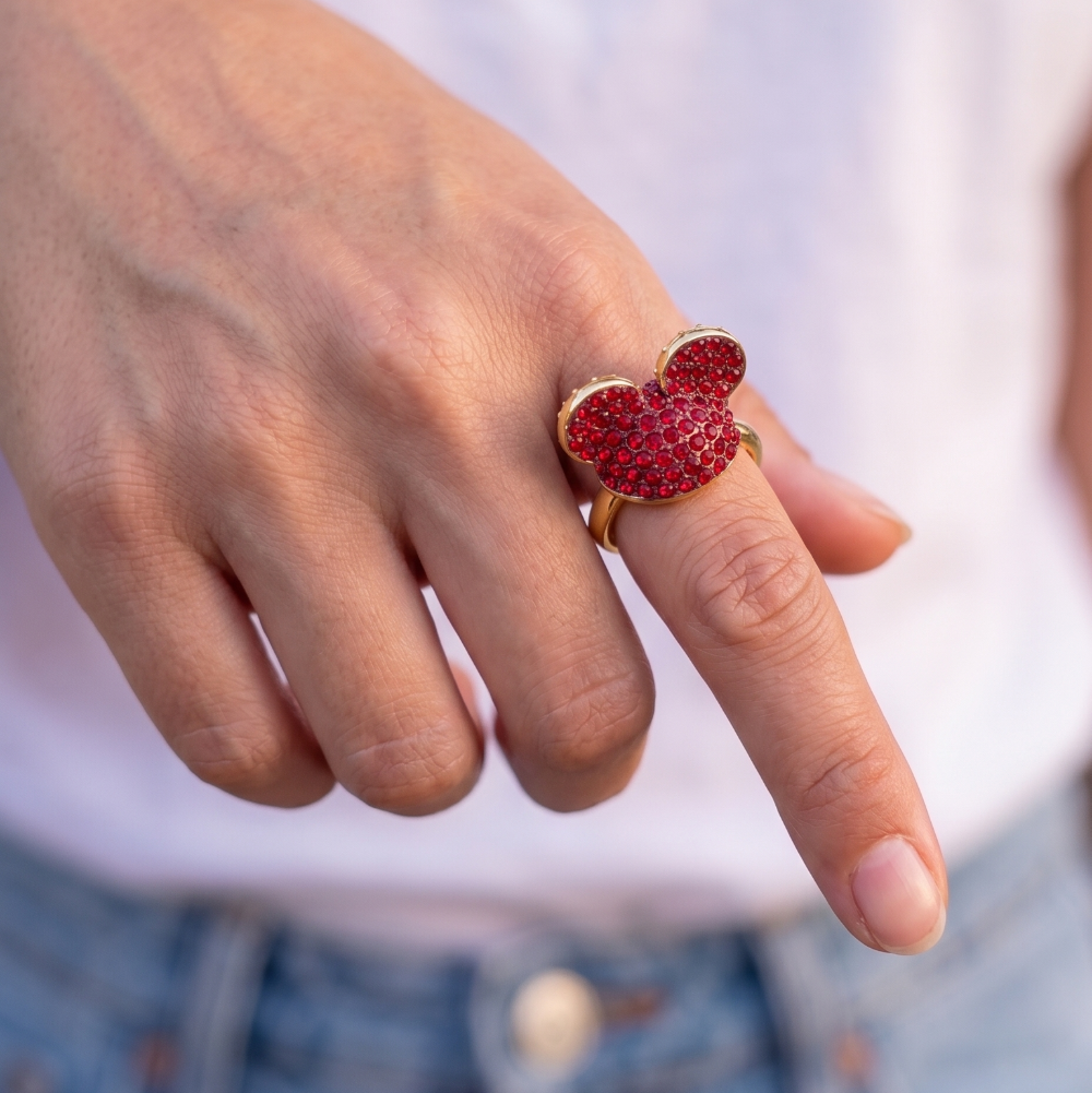 Hand wearing a gold ring with red crystal Mickey Mouse ears with a blurred background by Couture Kingdom