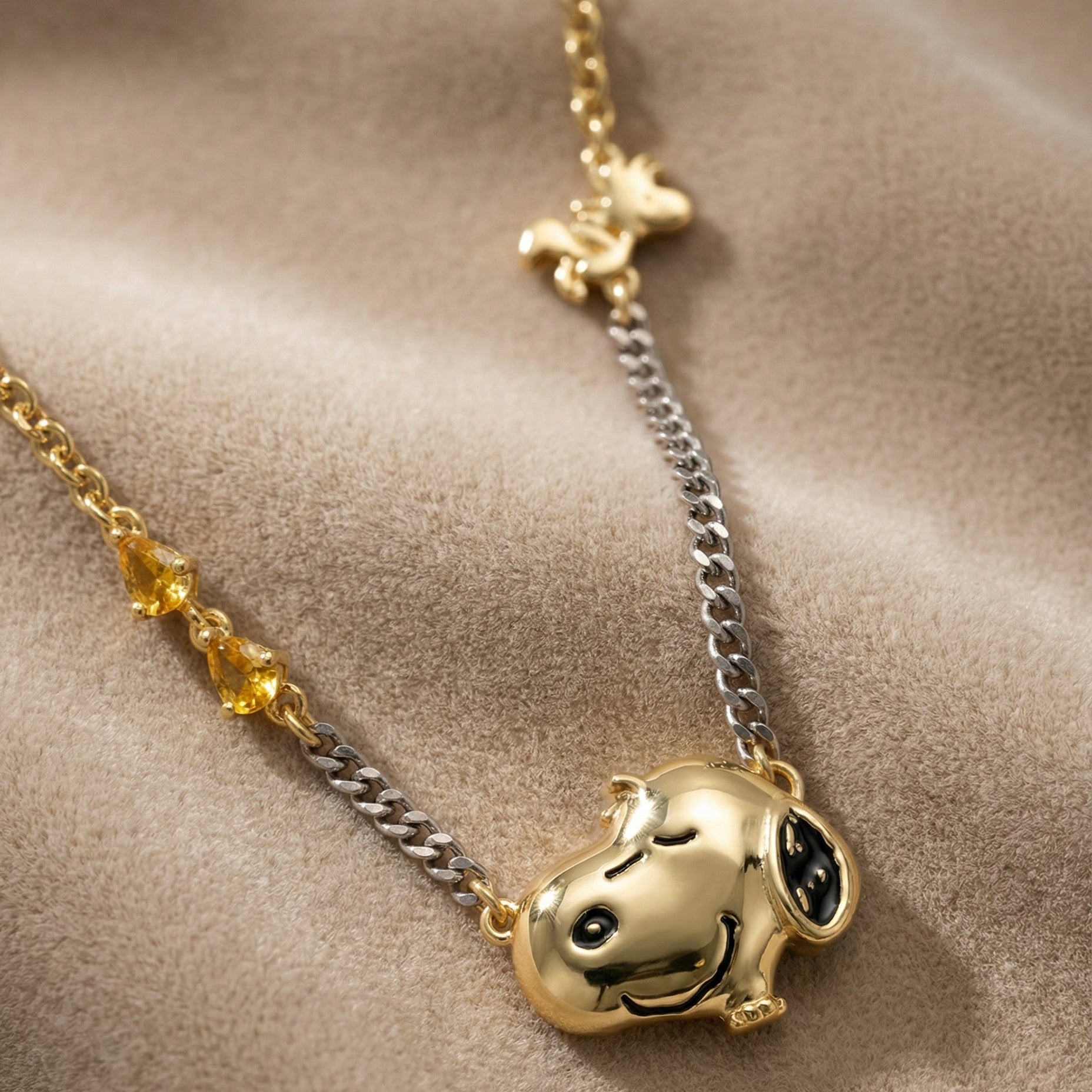 Gold necklace with Snoopy head pendant on a beige fabric background