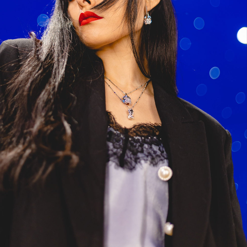 Person wearing a black coat with a blue crystal Marvel thanos necklace and earrings with blue starry background