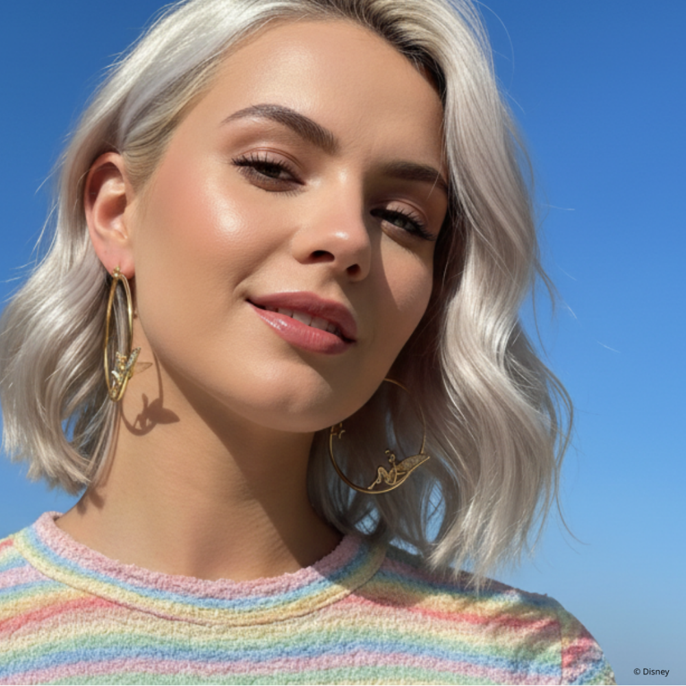 Woman with light-colored hair and a colorful striped sweater against a blue sky wearing yellow gold Disney Tinker Bell Hoop Earrings by Couture Kingdom