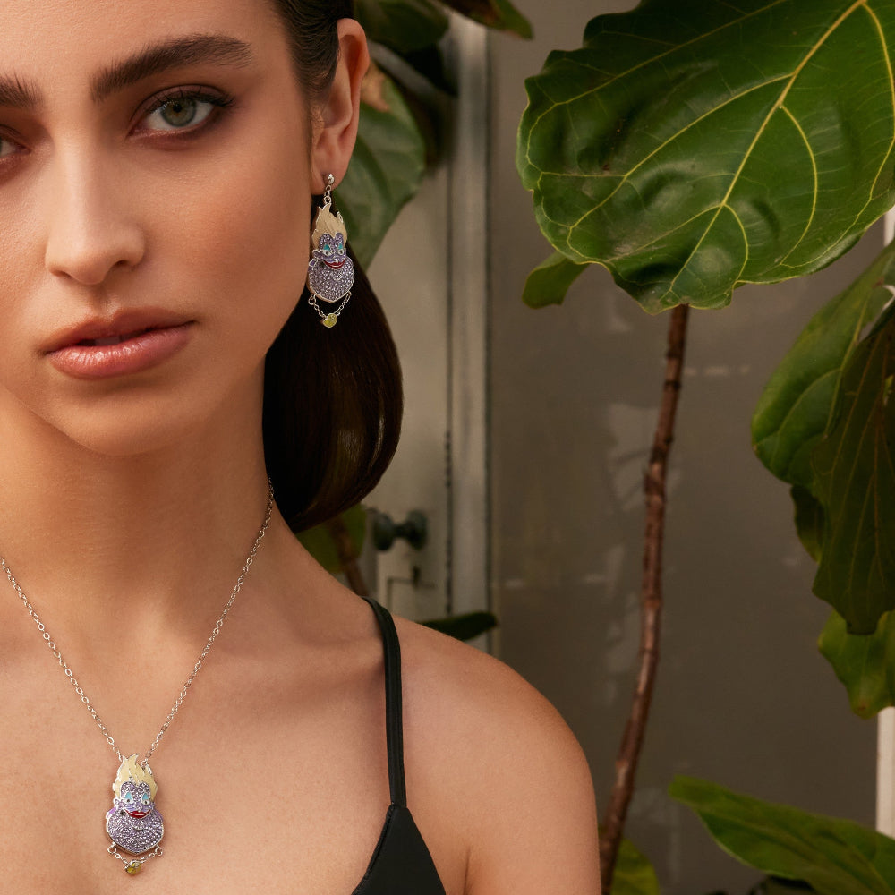 White Gold Disney Villains Ursula Drop Earrings with purple crystals and matching necklace by Couture Kingdom worn on model with green leafy background